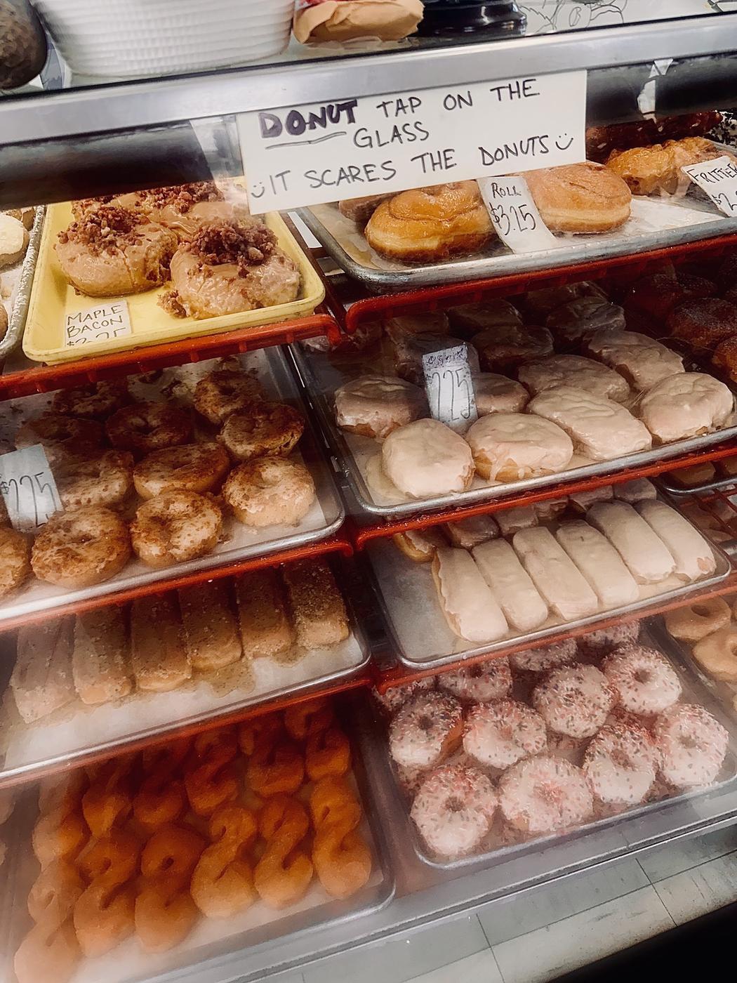 The display case at World's Fair Donuts, trays of donuts stacked behind glass, with a handwritten sign taped to the front