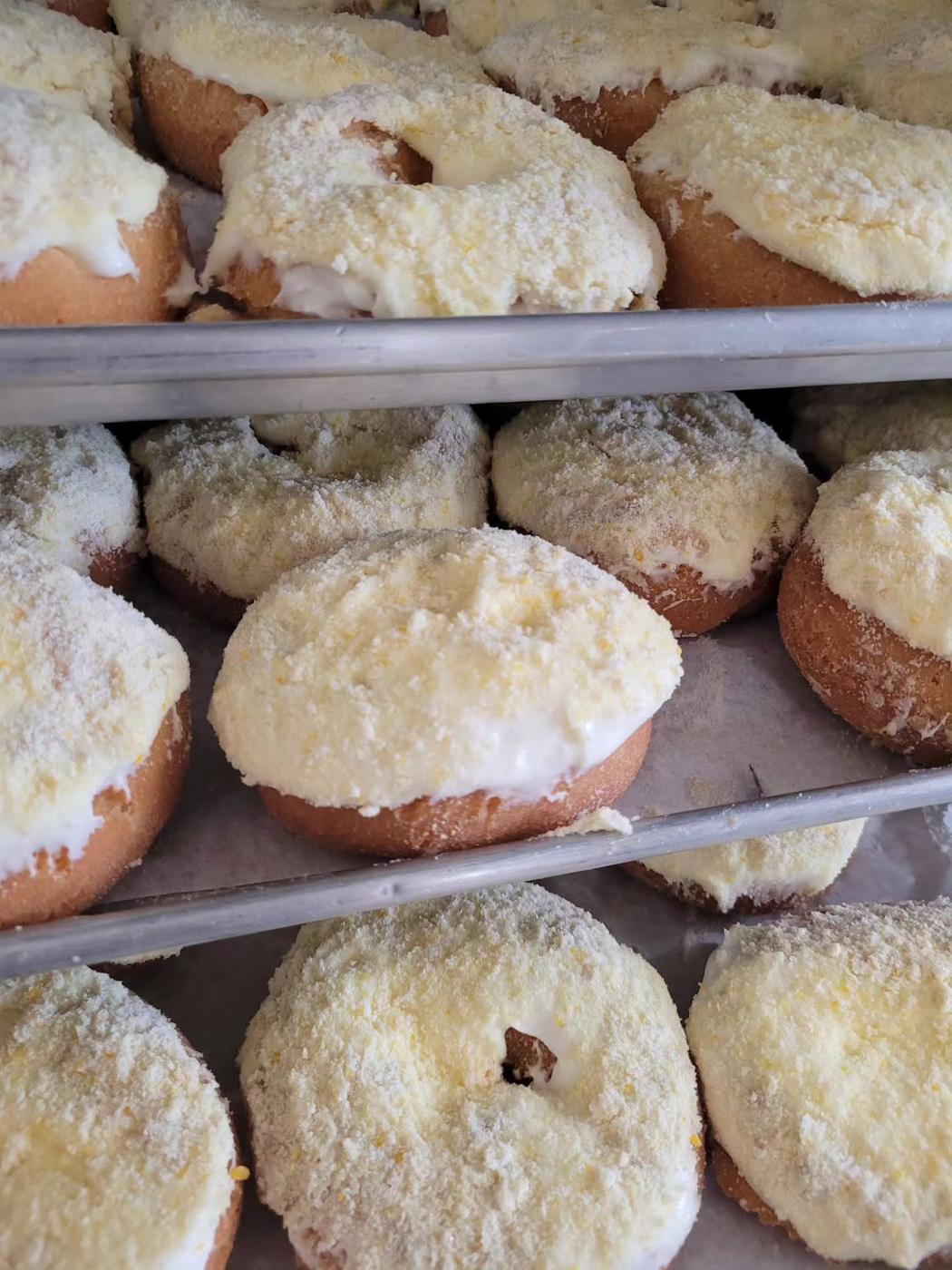 Trays of gooey butter cake donuts at World's Fair Donuts, topped with streusel and powdered sugar, stacked on racks