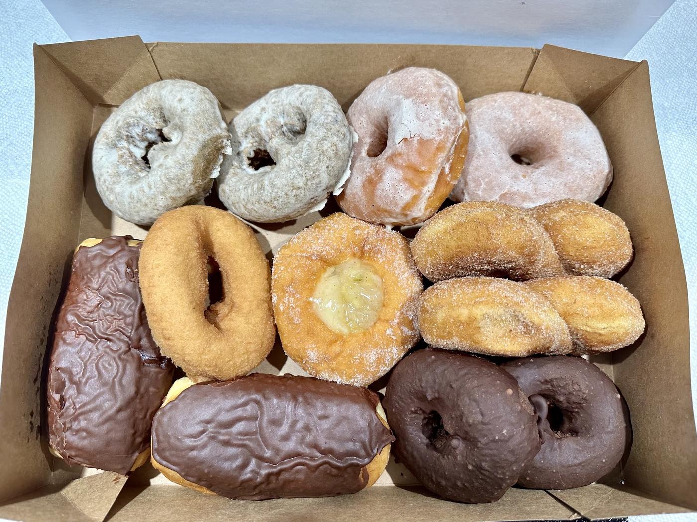 An open box of a dozen donuts from World's Fair Donuts: powdered cake rings, glazed, cinnamon sugar, chocolate long johns and chocolate iced rings